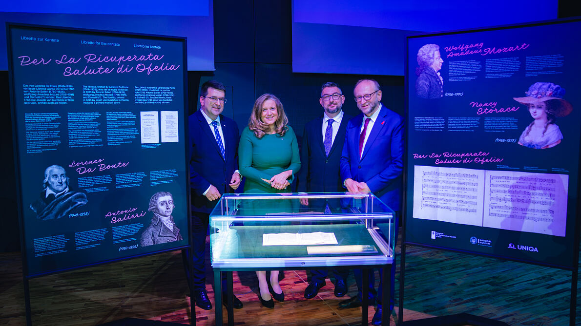 Vier Personen stehen vor Ausstellungsstücken mit Noten und Porträts von Lorenzo Da Ponte.
